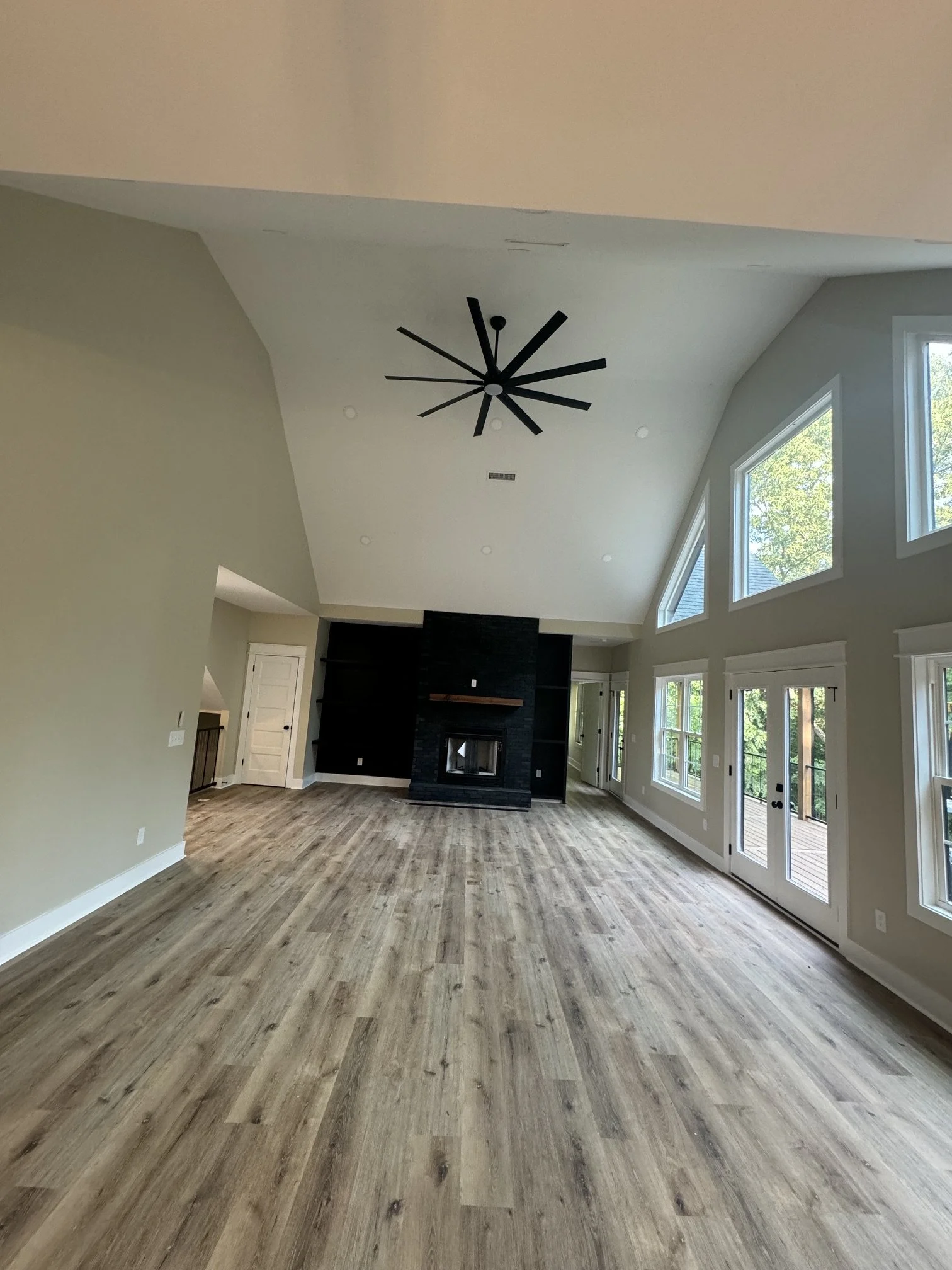 Spacious living room with high vaulted ceilings, large windows, hardwood floors, and a black fireplace.