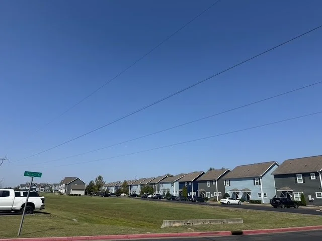 Residential neighborhood with several two-story houses, parked cars, and a clear blue sky.