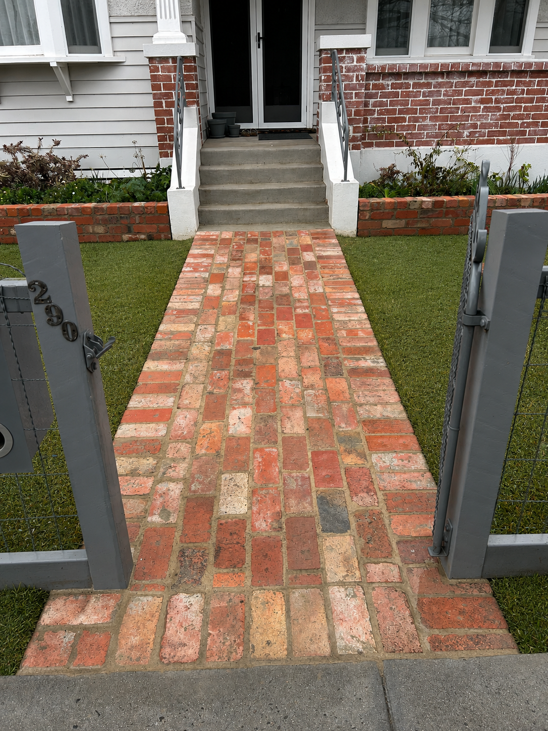 Reclaimed brick front pathway with garden beds leading to the entrance of a home.