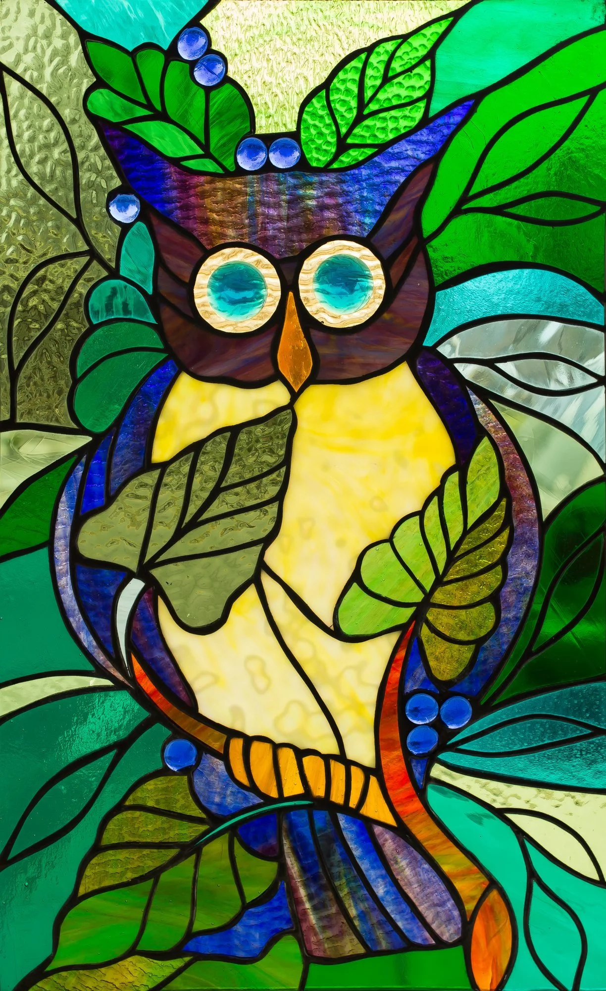 A stained-glass owl with blue eyes, yellow plumage, and green leaves.