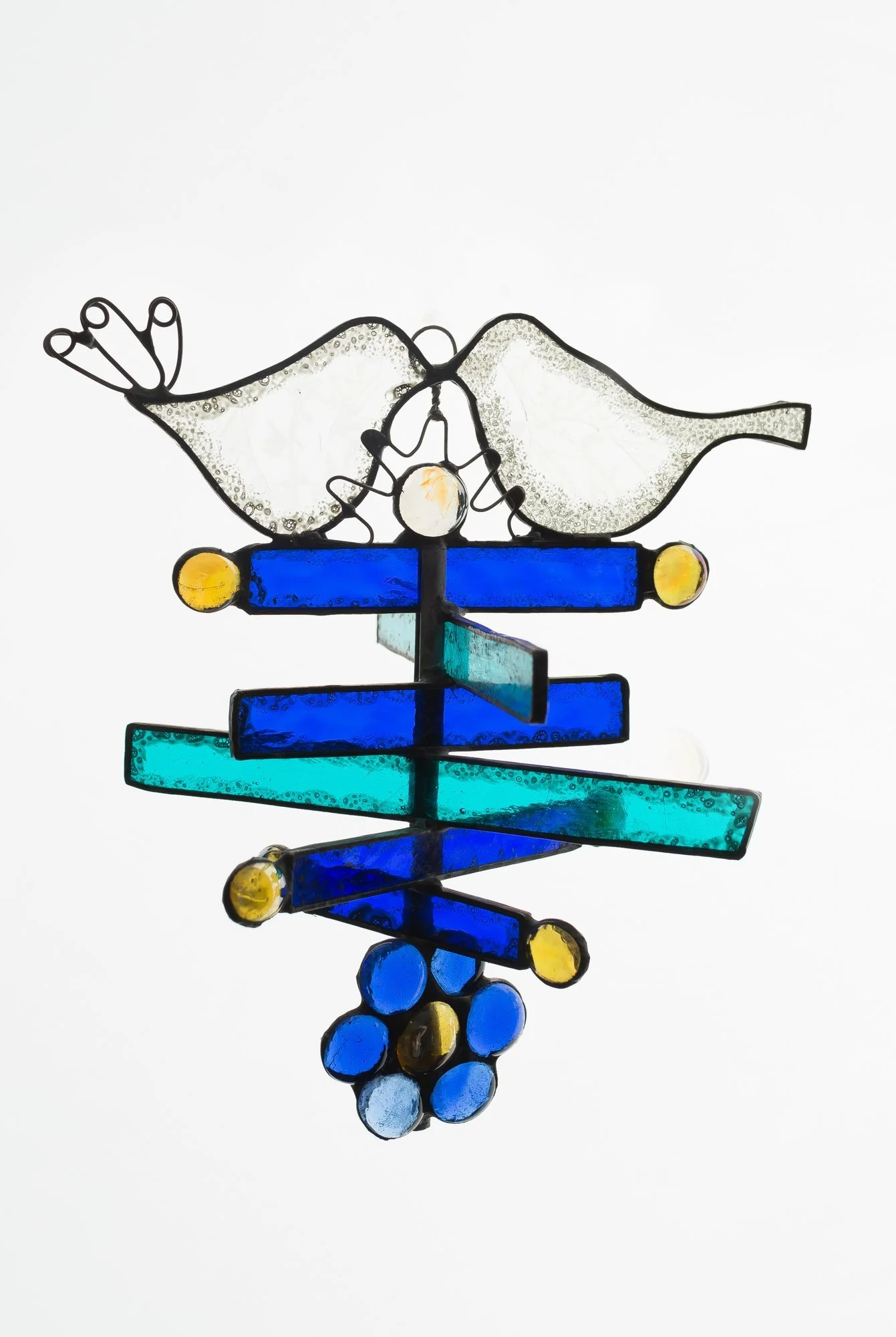 A hanging glass piece with two white birds above horizontal blue strips and colored glass jewels.