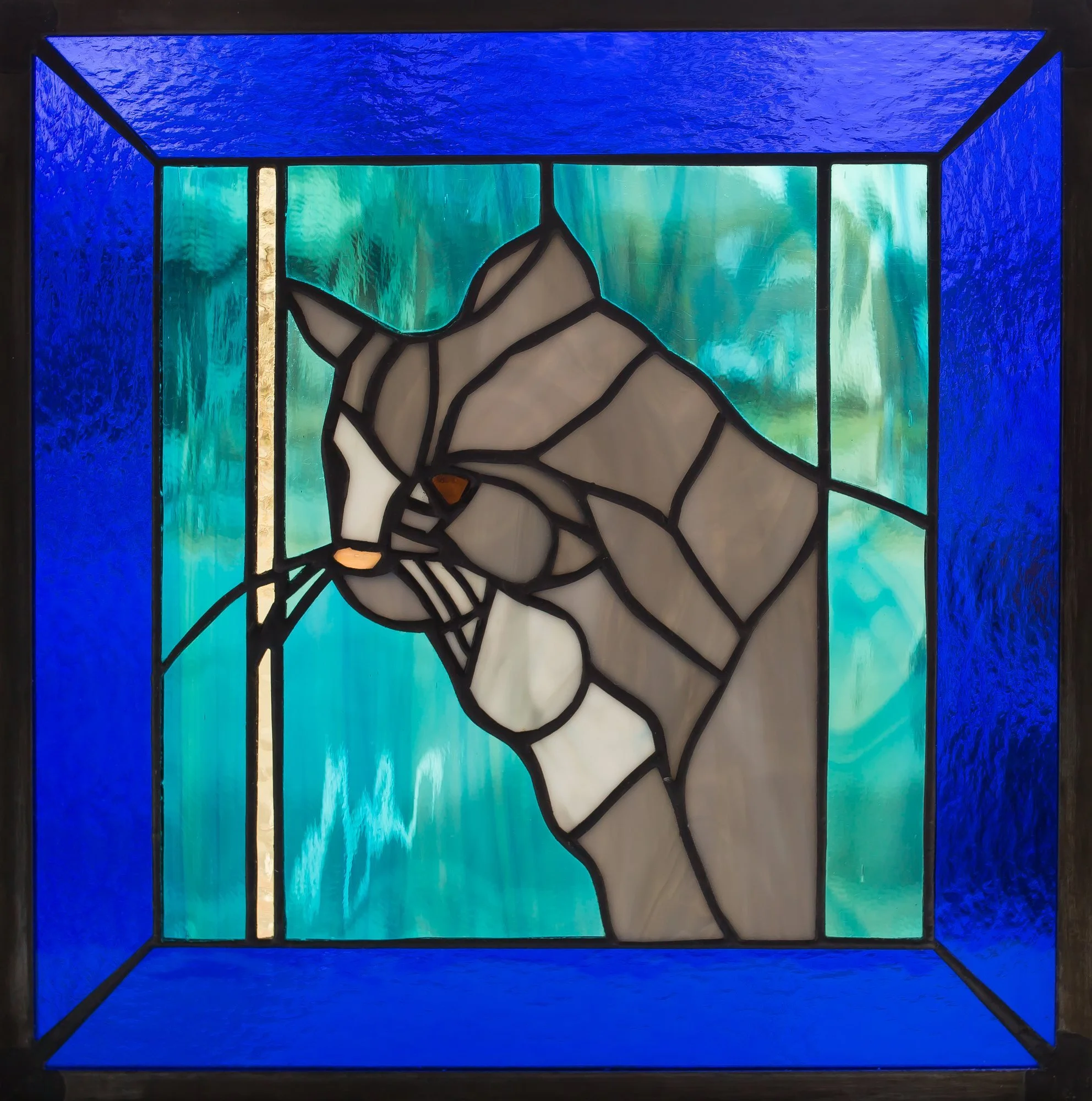 A stained-glass cat in profile against turquoise glass, framed in deep blue.