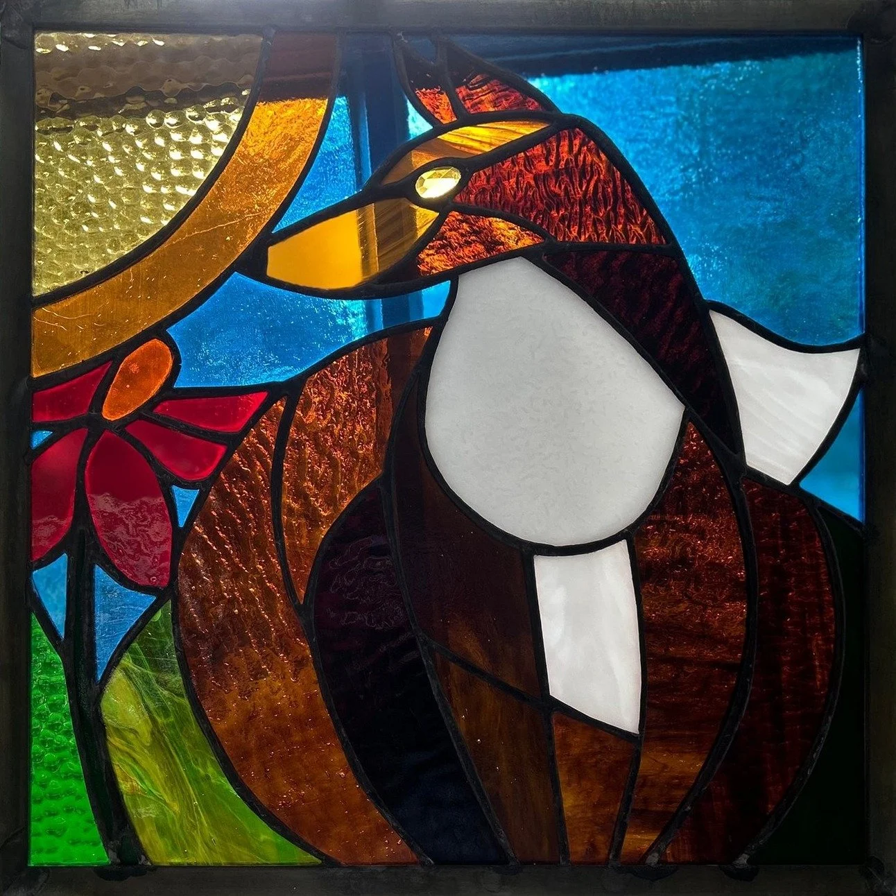 A brown and amber stained-glass fox with a white chest sits beside a red flower beneath a golden sun.