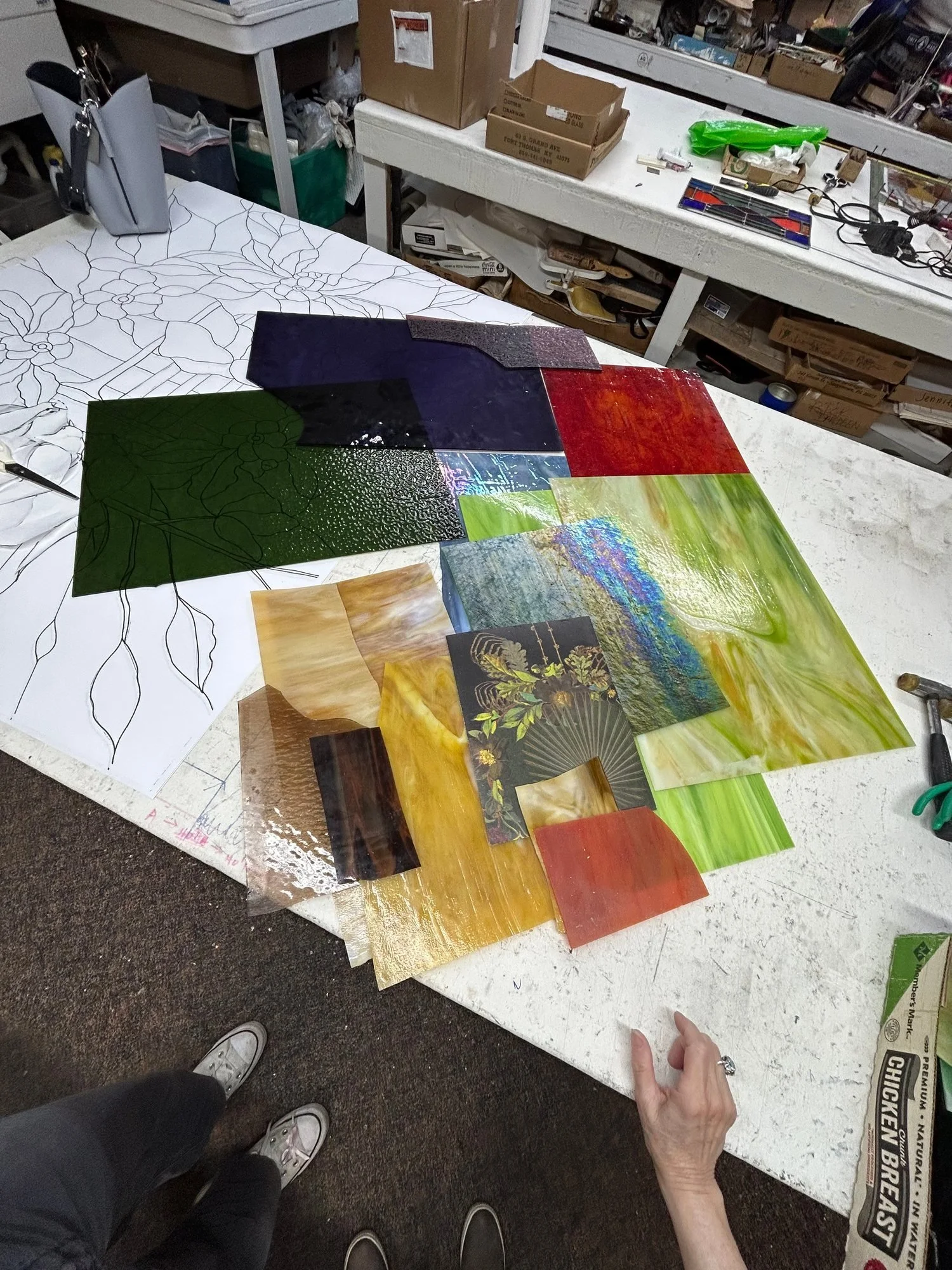 Colored glass samples arranged on a worktable beside the matching drawn floral pattern.