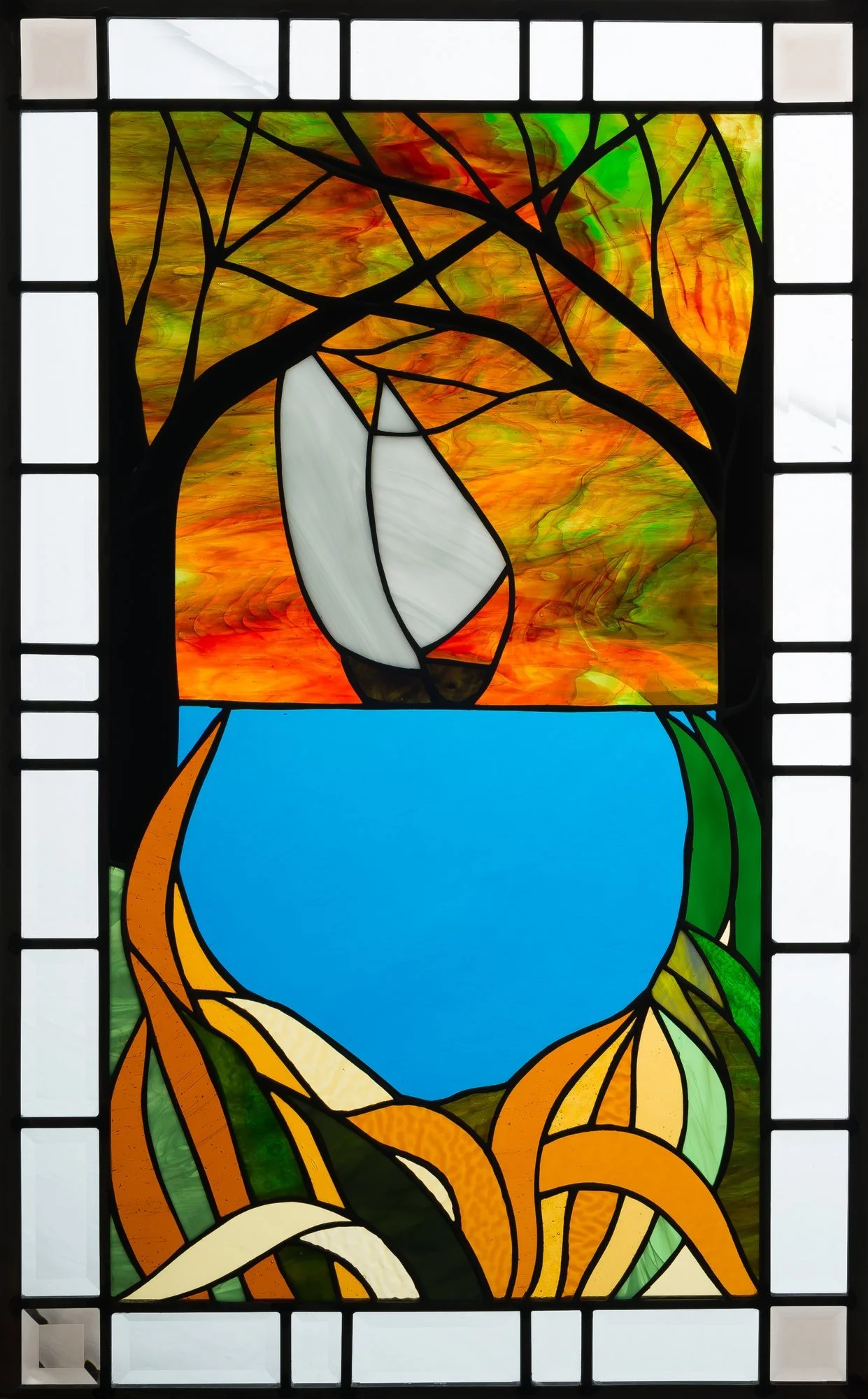 A white sailboat on blue water beneath golden leaves in a framed stained-glass window.
