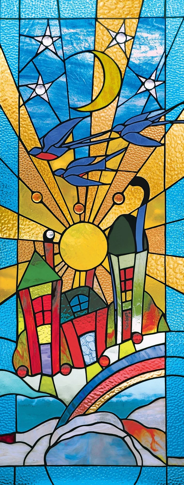 A tall stained-glass design with a rainbow, colorful buildings, flying birds, a sun, moon, and stars.