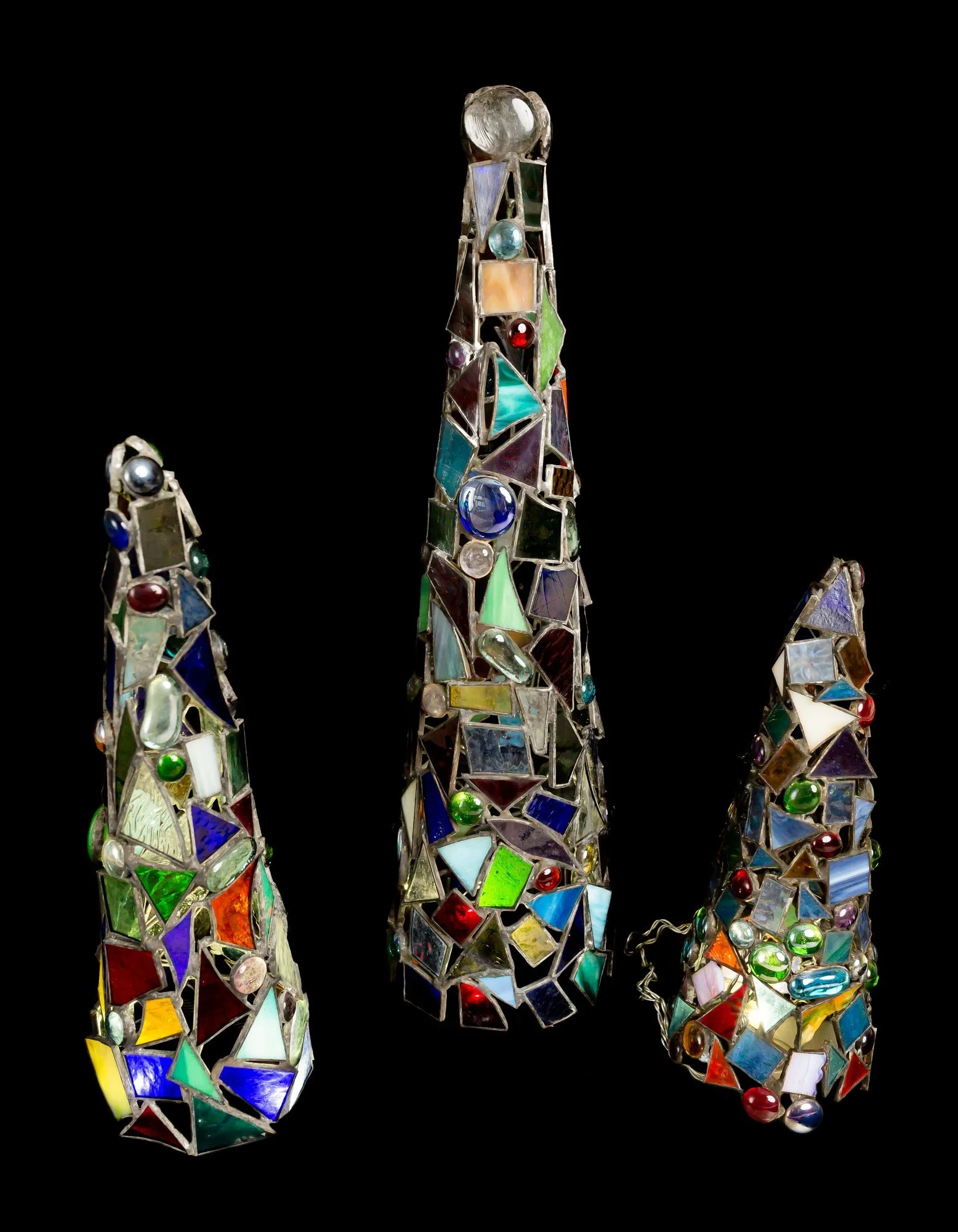 Three decorative stained-glass trees made with multicolored glass pieces against a black background.