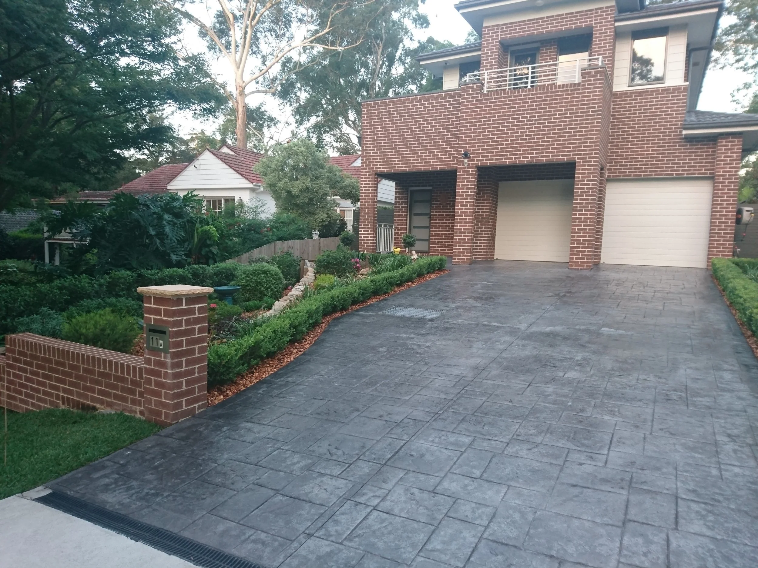 View of a modern brick house with a concrete driveway, garage doors, and landscaped garden.