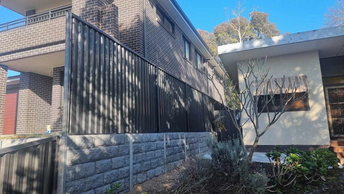 Residential building with brick walls, a balcony, and a modern extension with a tree and plants in the front yard.