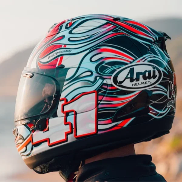 Close-up of a motorcycle helmet with a colorful flame design, the Arai logo, and a red outline of a race track.