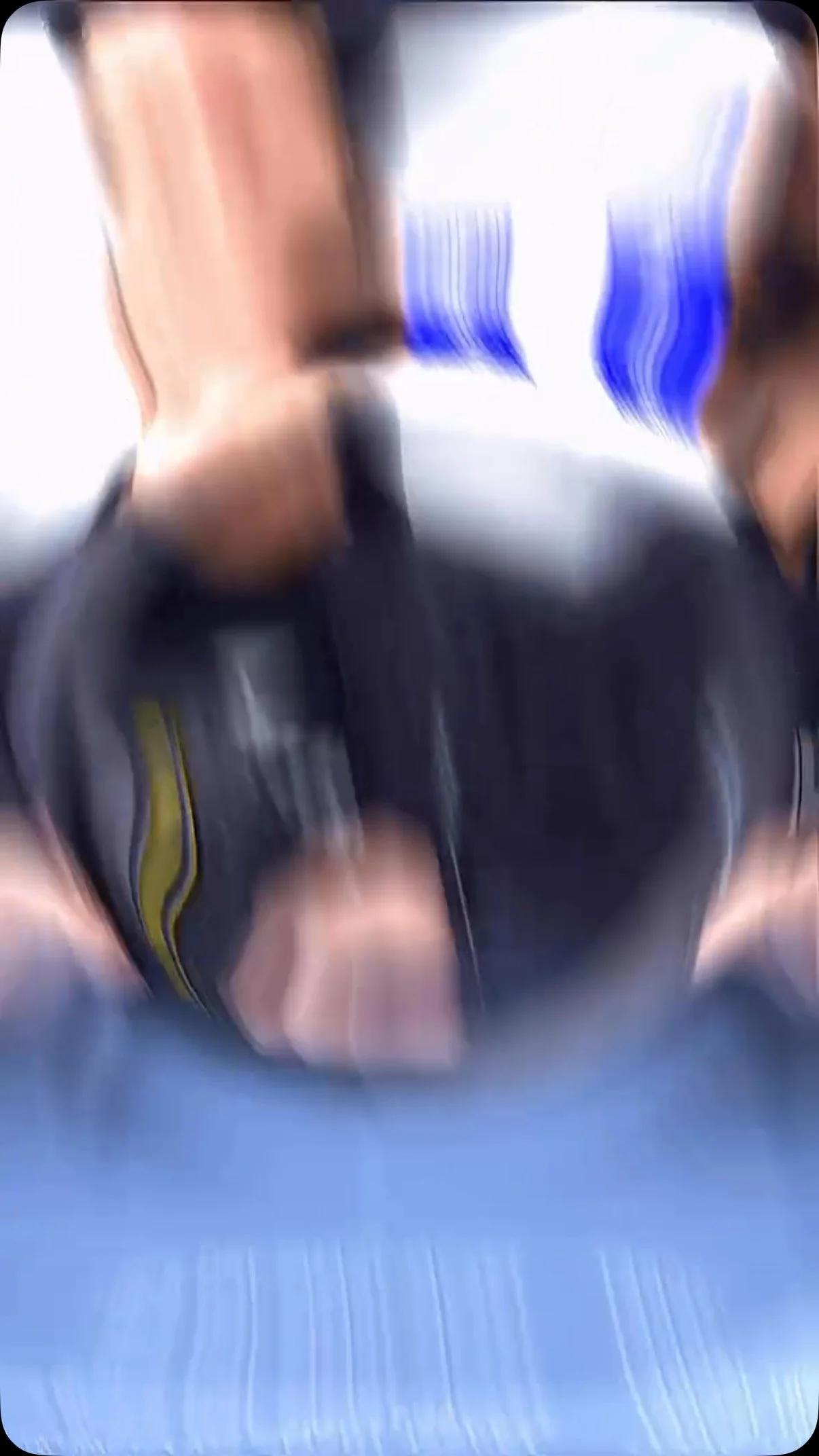 A distorted, blurry image of a person holding a phone, with a blue surface underneath. The person seems to be taking a photo or video.