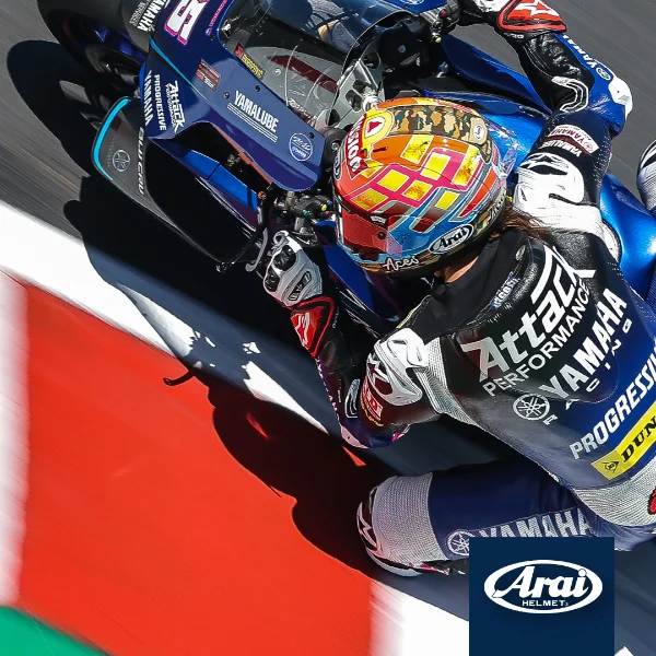 A motorcycle racer in a black and white racing suit, with a colorful helmet, leaning into a corner on a Yamaha motorcycle during a race.