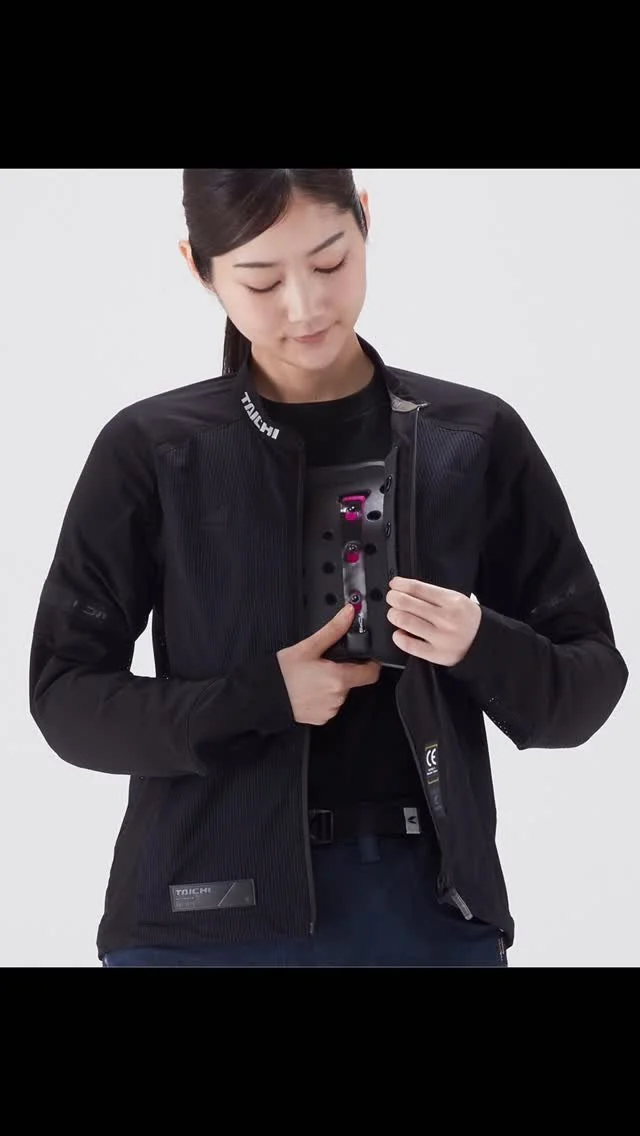A woman in a black jacket is holding and examining a black electronic device with pink accents