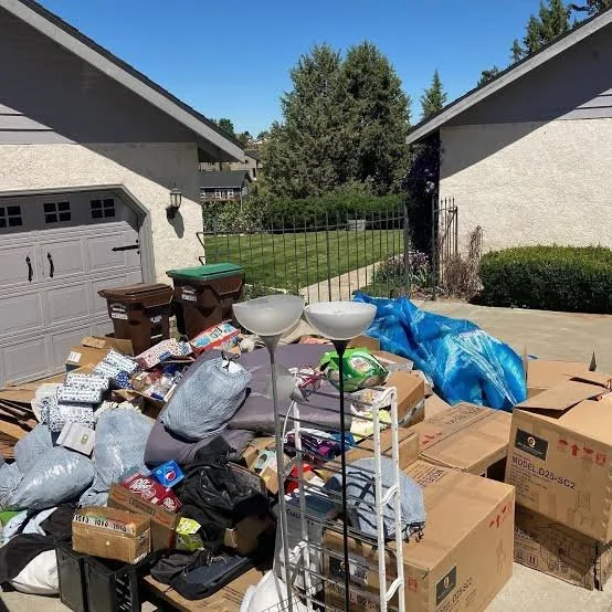 Overflowing outdoor trash area with boxes, bags, and household items in a driveway.