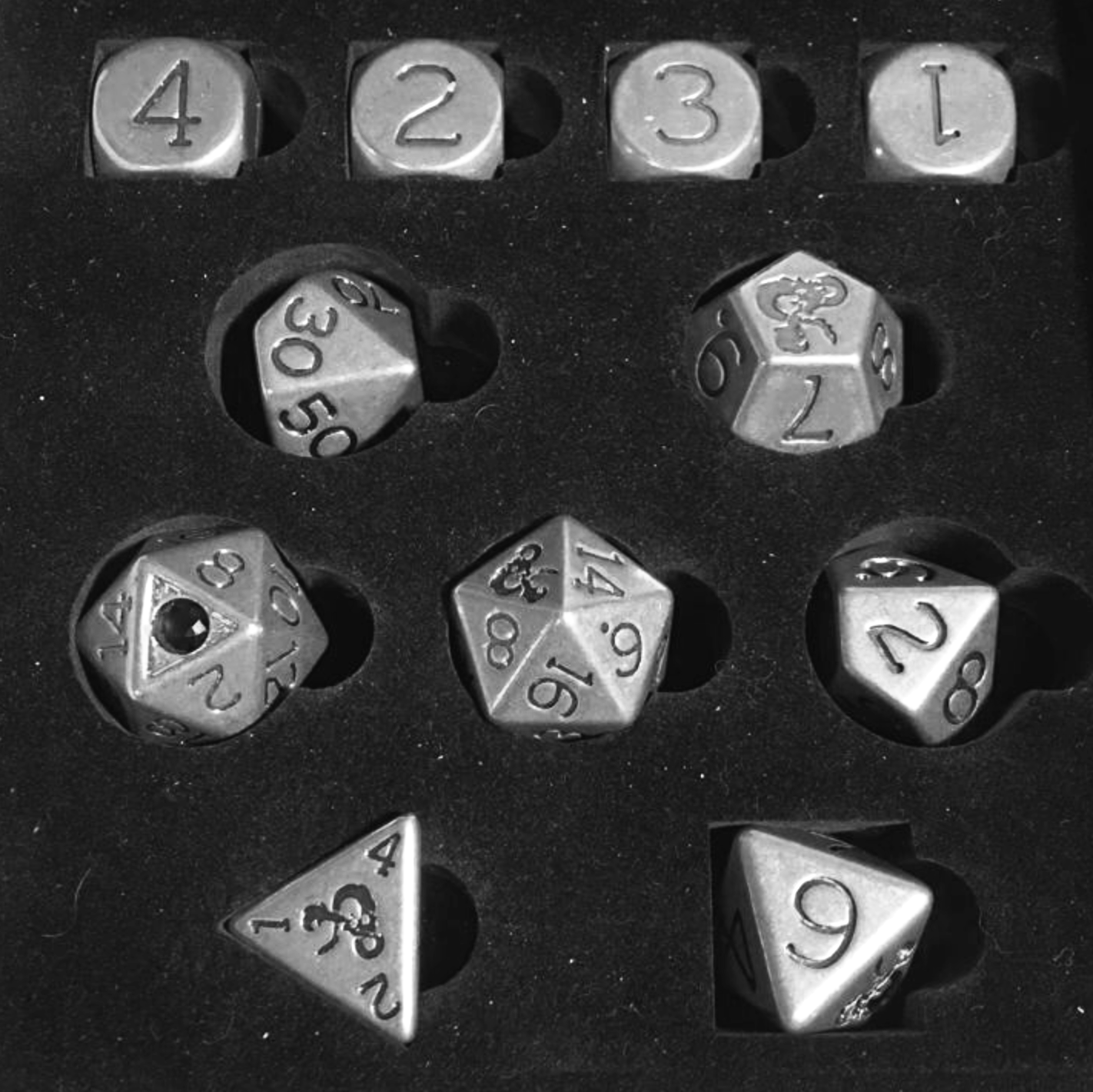 A collection of metallic role-playing game dice in a foam tray, including a four-sided die, a six-sided die, an eight-sided die, a ten-sided die, a twenty-sided die, and a twelve-sided die, all with engraved numbers.