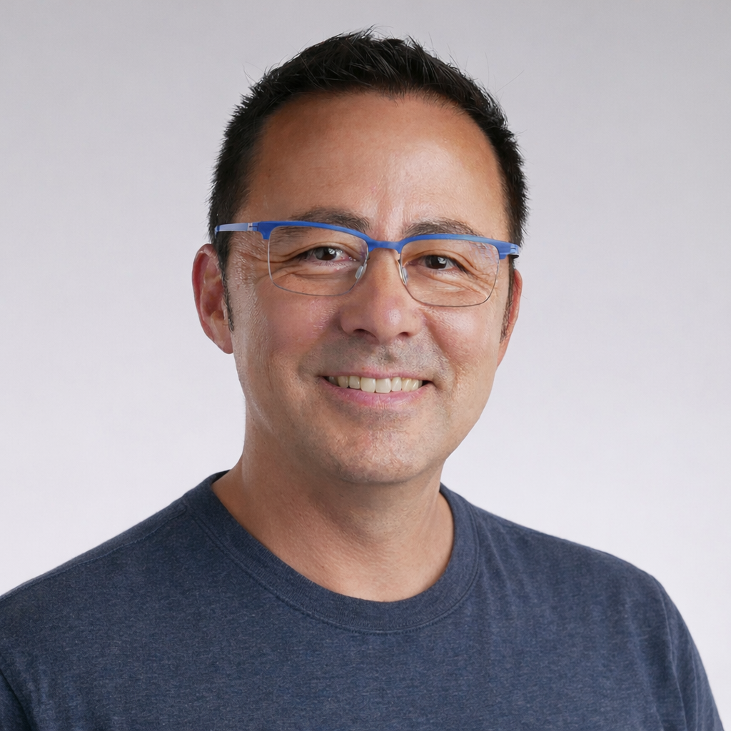 A middle-aged man with short dark hair, wearing glasses with blue frames, smiling and looking at the camera against a plain white background.