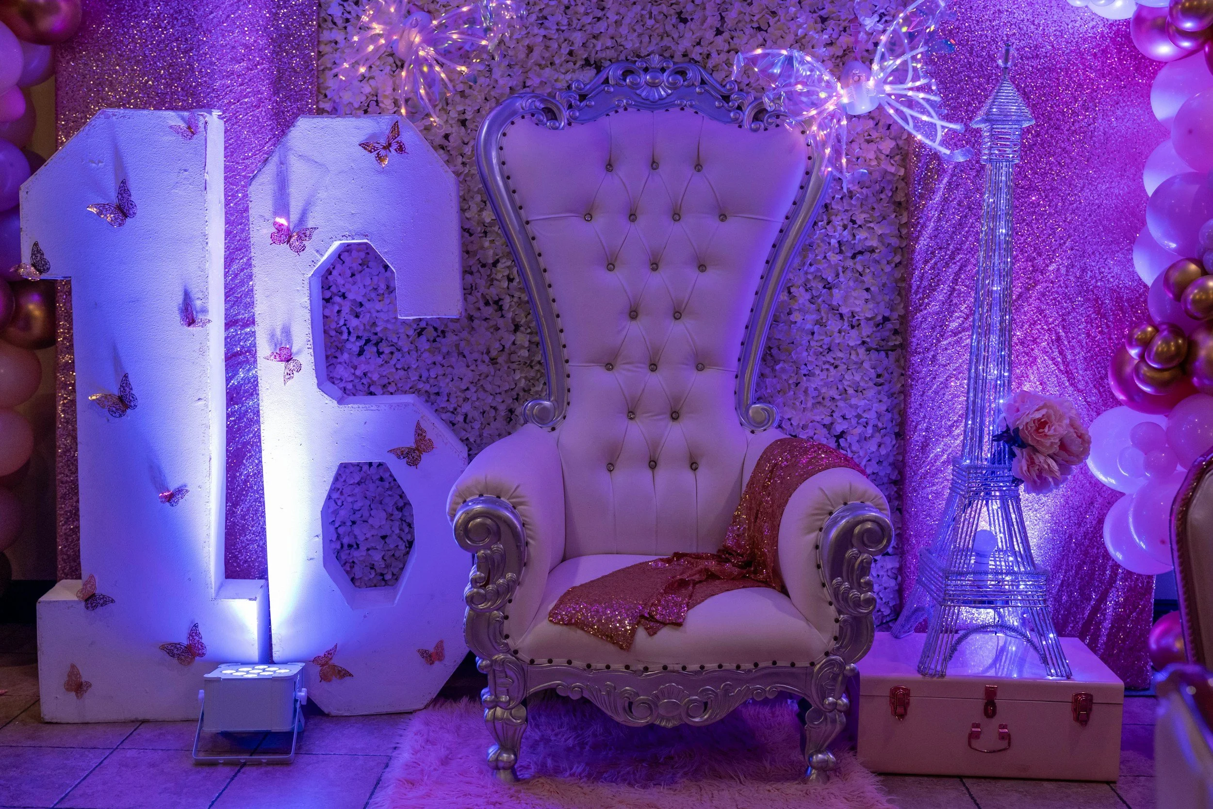 Decorated Sweet 16 milestone display with number sixteen, throne chair, and purple uplighting