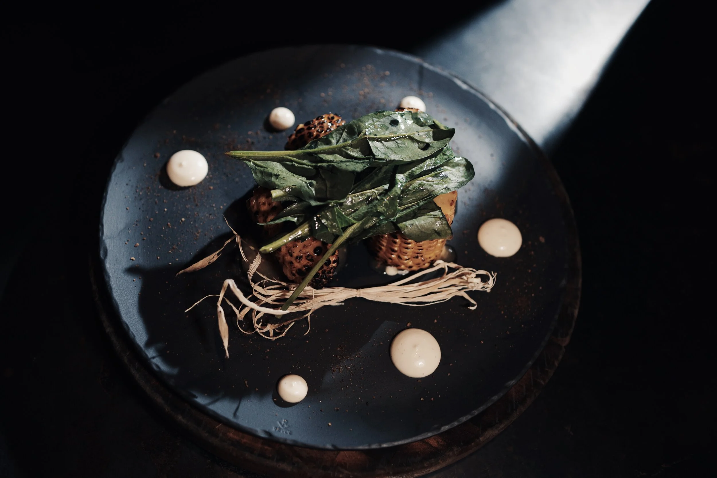 Gourmet dish with grilled corn, greens, and sauce on a dark plate