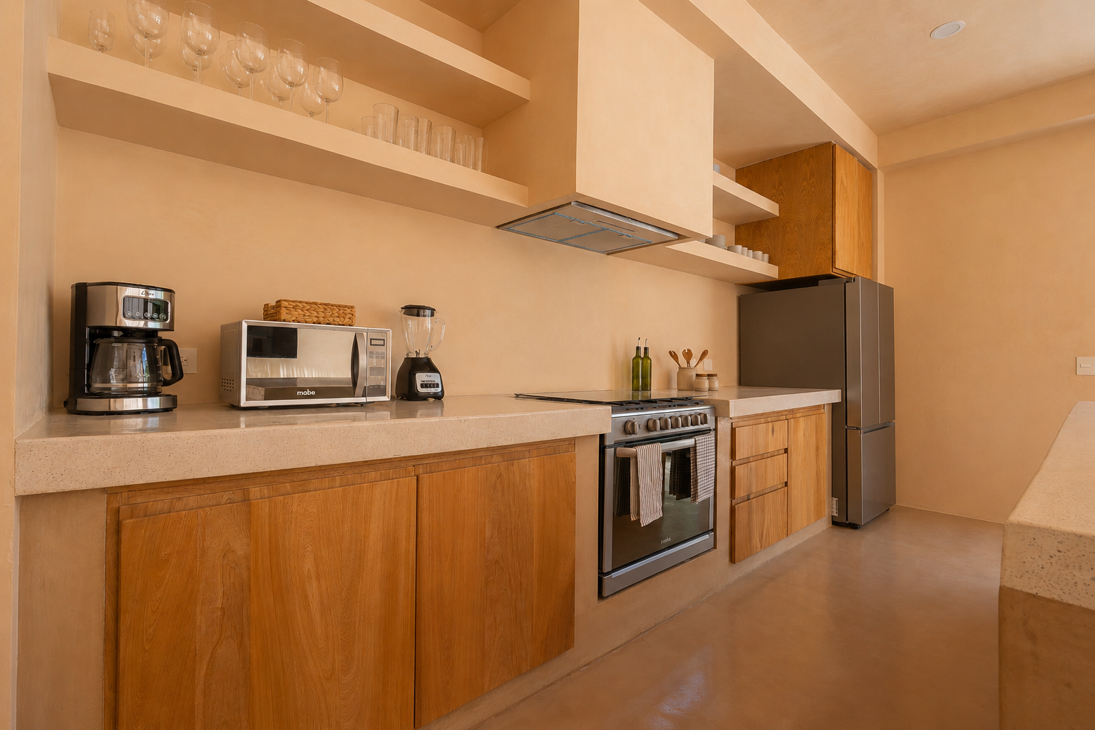 Kitchen with wooden cabinets, a stainless steel refrigerator, a stove, a microwave, a coffee maker, and a blender on a beige countertop. Wall shelves hold glassware and cups.