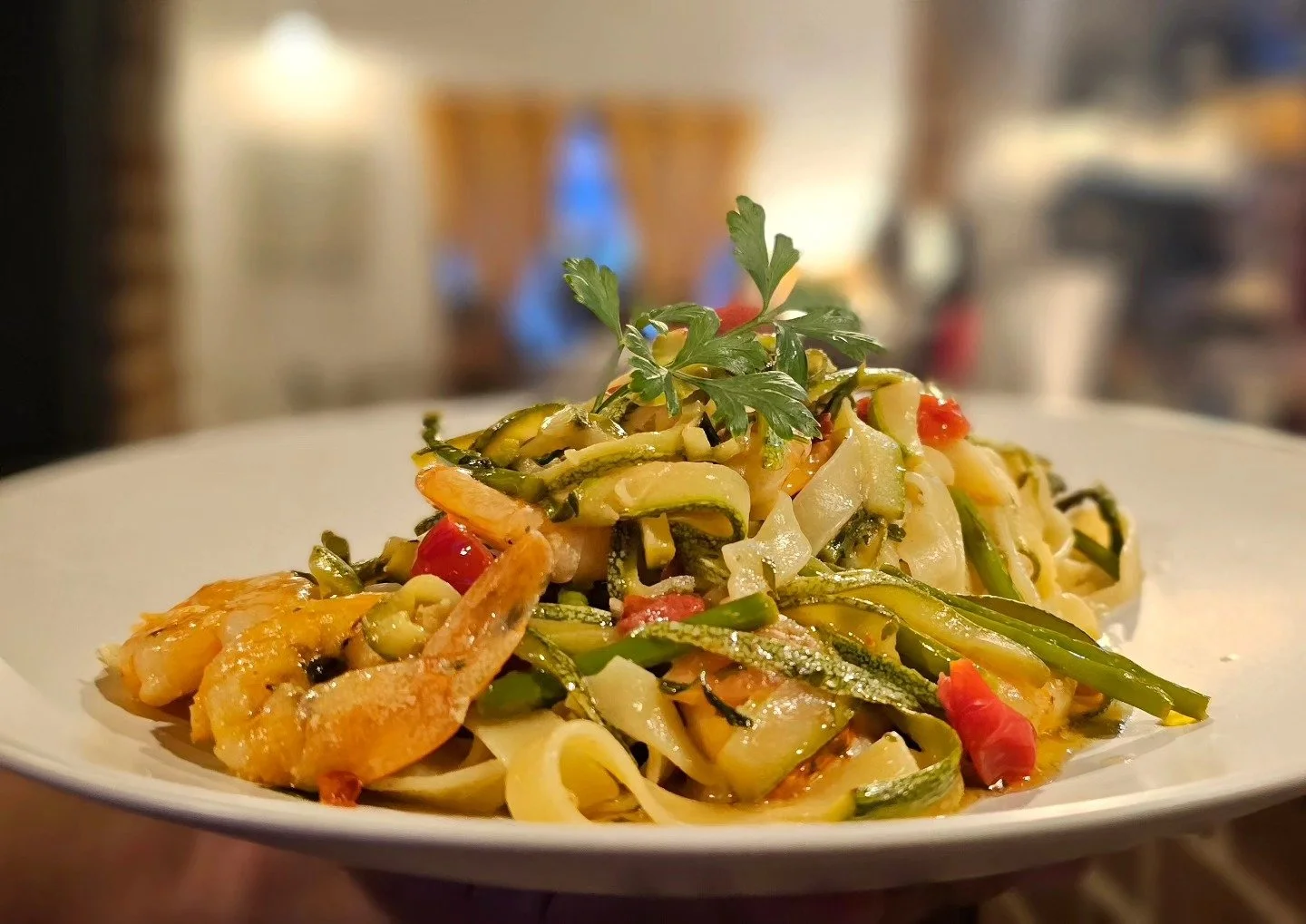 Fried shrimp noodle dish with vegetables and garnished with parsley on white plate