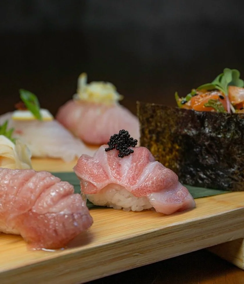 Close-up of assorted sushi, including slices of raw fish, garnished with caviar and greens, on a wooden sushi platter.