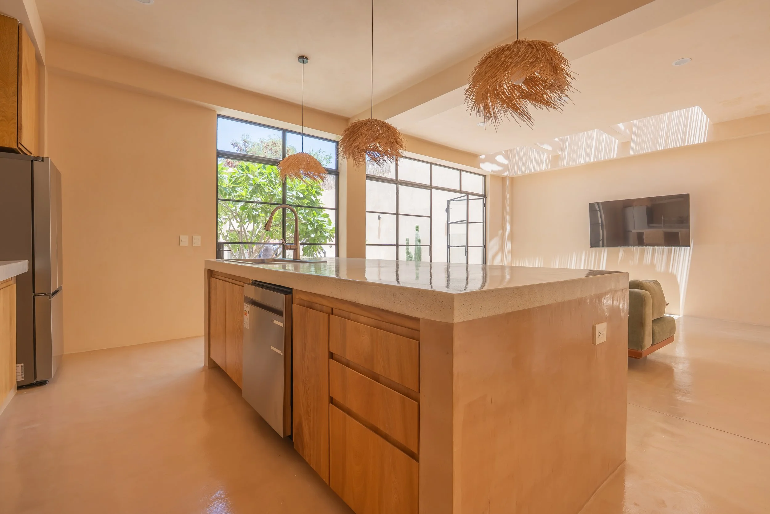 Modern kitchen with a large island, pendant lights, and large windows with greenery outside.