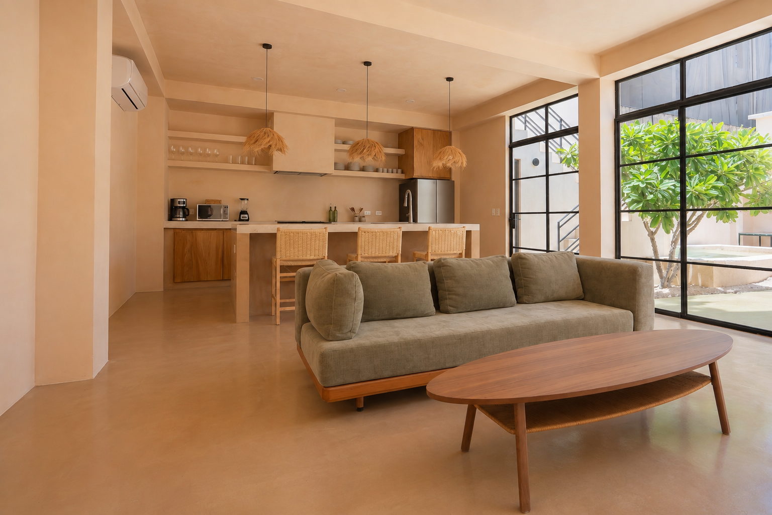 Open-concept living room and kitchen with beige walls and furniture, large glass sliding doors revealing an outdoor patio and greenery.