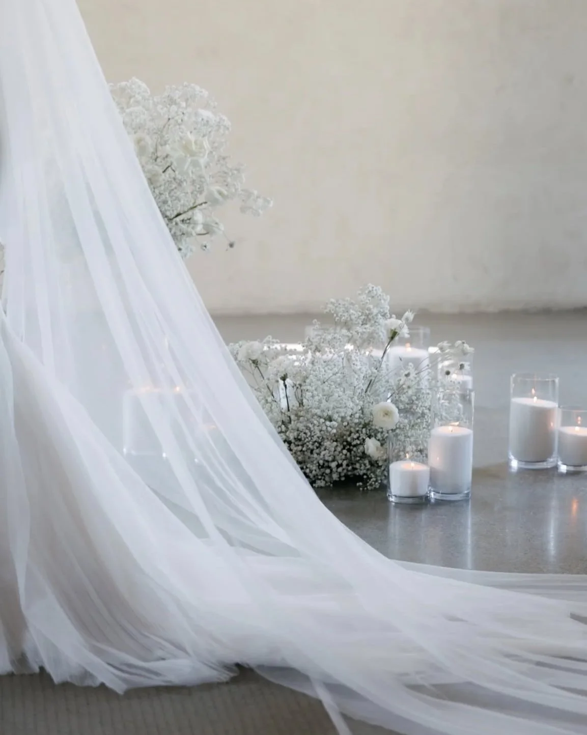 A wedding setup with white floral arrangements, candles in glass holders, and a flowing white veil or fabric.