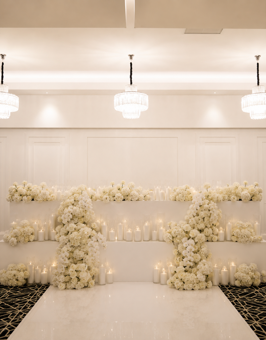 White floral wedding altar decorated with white flowers and candles in a luxurious banquet hall illuminated by elegant chandeliers.