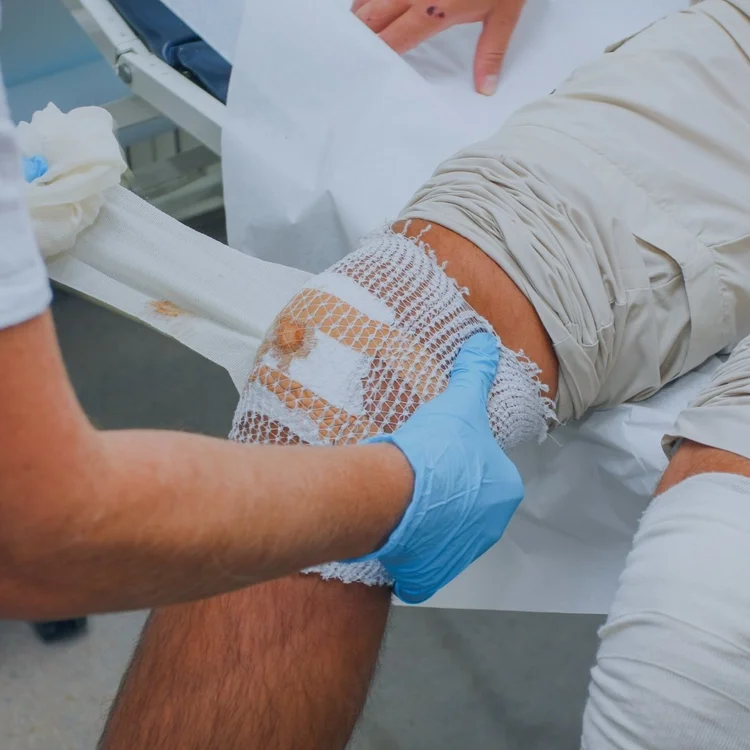 Clinician securing a fresh dressing over a bandaged wound on a patient’s leg