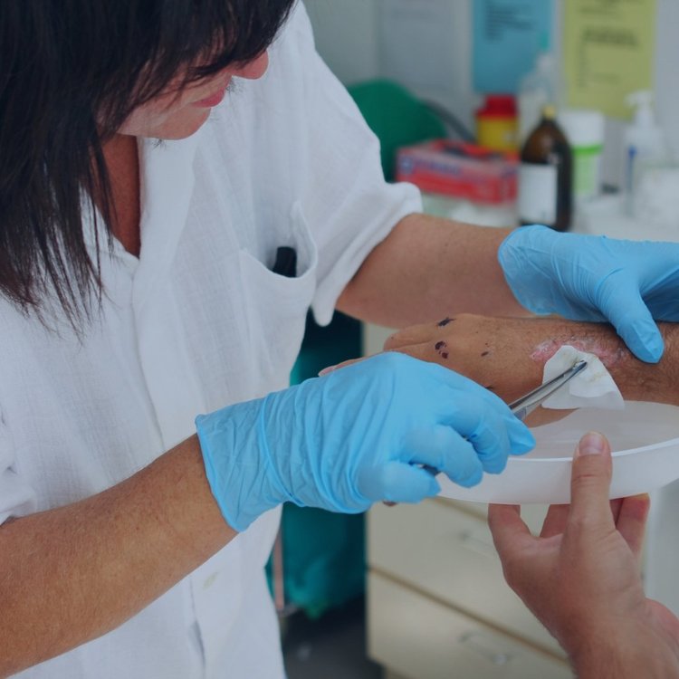 Clinician in scrubs cleaning a wound on a patient’s forearm