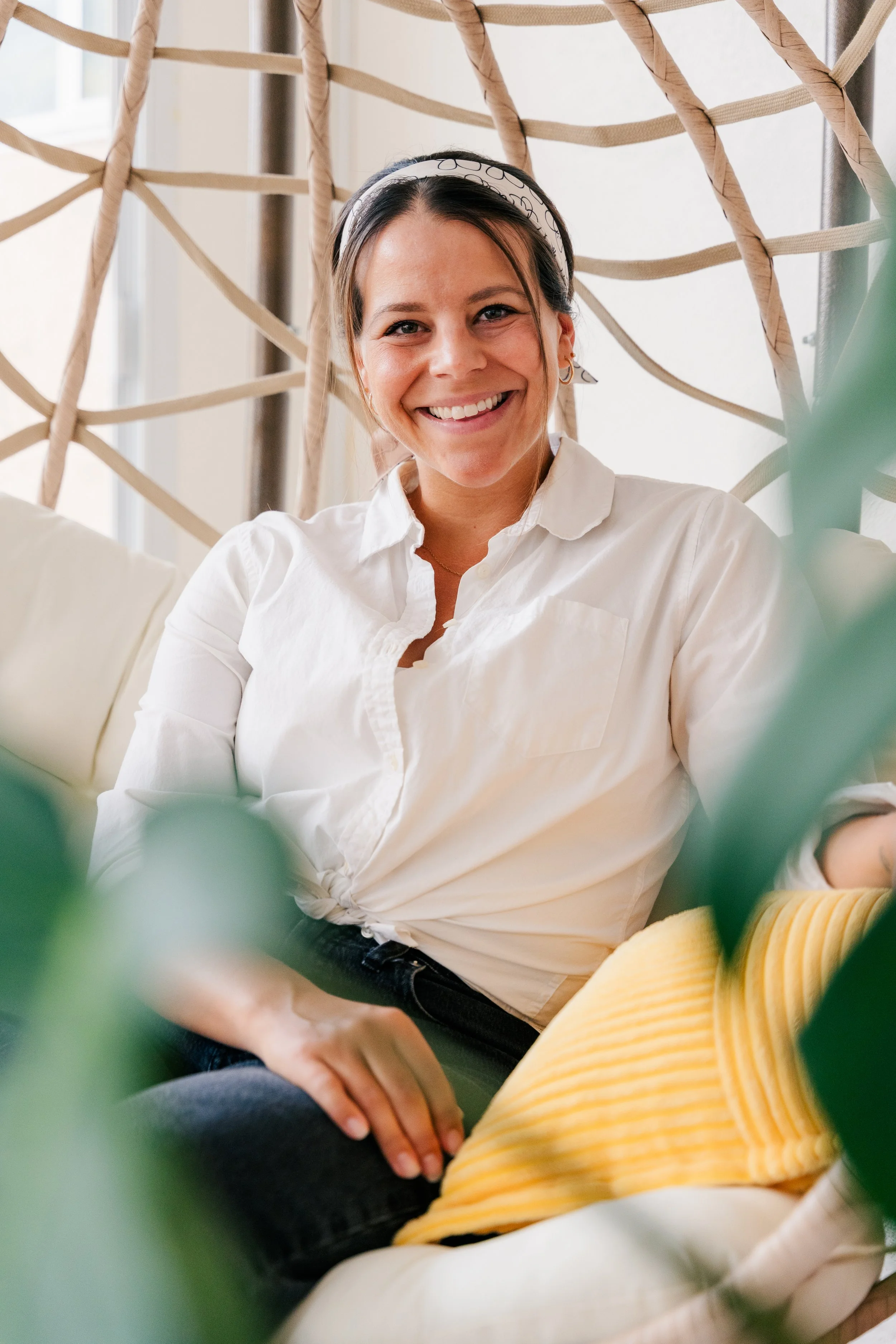 Smiling woman with dark hair, wearing a white shirt and a headband, sitting beside someone in a yellow striped shirt, with a woven background and natural light coming through a window.
Therapist, smiling, warm, friendly, open