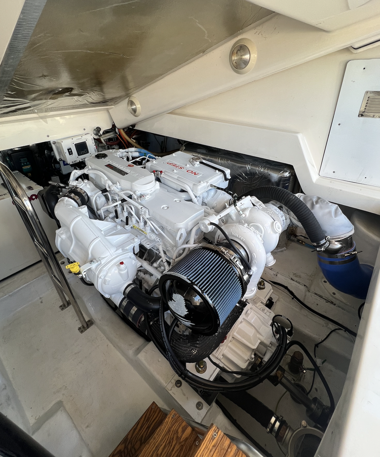 Marine engine inside a boat engine compartment, white in color with a large air filter and various pipes and cables.