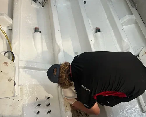 Person working inside a white boat, kneeling and using tools near the interior.