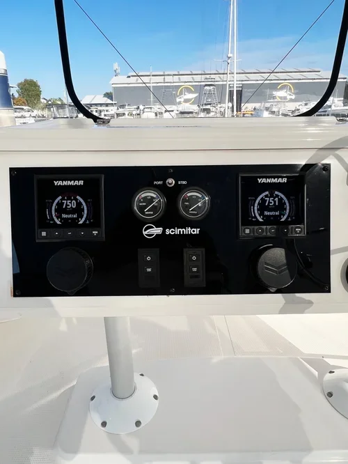 Boat dashboard with Yanmar navigation screens, analog gauges, and control switches, with a marina and other boats in the background.