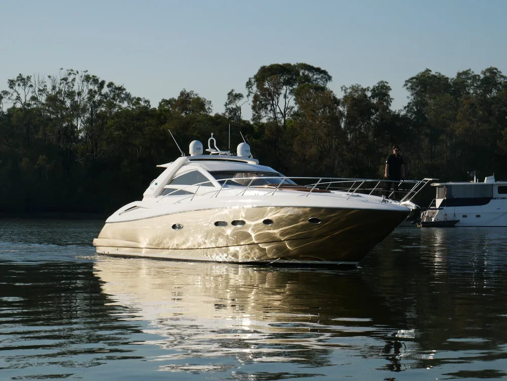 A luxurious white yacht on calm water with trees in the background and a person standing on the deck.
