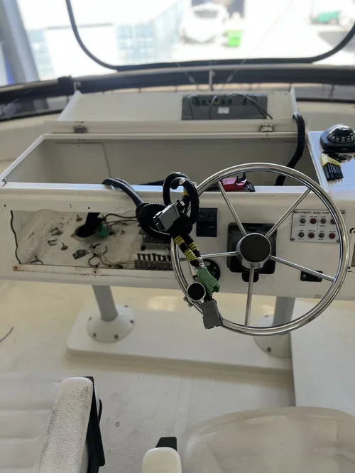 A boat's control console with a steering wheel, electronic panel, and wires, with some parts missing or disconnected.