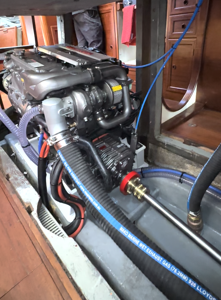 Marine engine installed on a boat with various hoses and wiring, inside a wooden cabin.