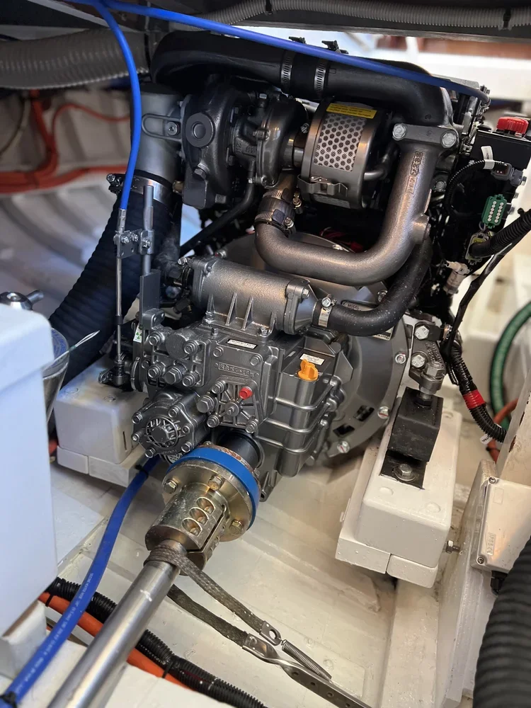 Close-up of a compact, industrial engine or machine with various metallic and plastic components, pipes, and wiring, mounted on a white platform.