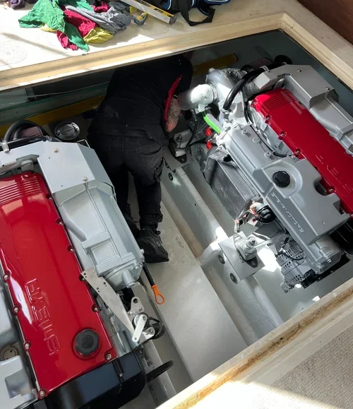 A person working on two large, red and gray marine engines inside a boat's engine compartment.