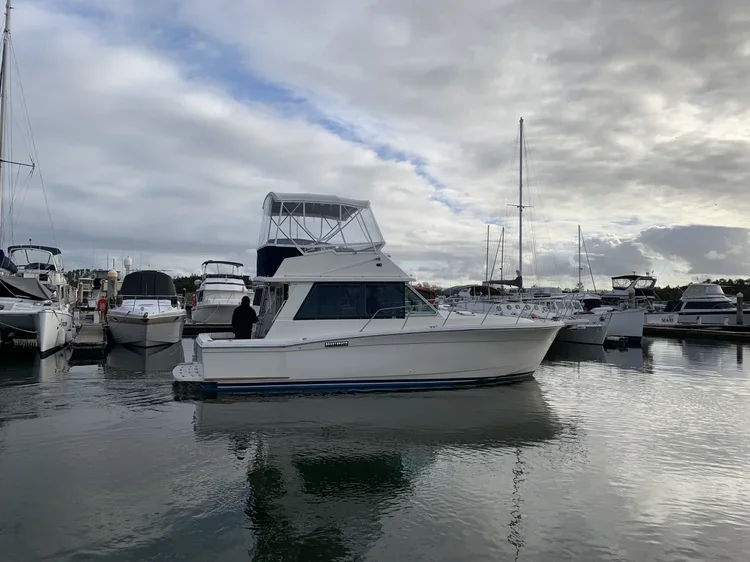 A white motorboat docked at a marina with several other boats surrounding it under a cloudy sky.