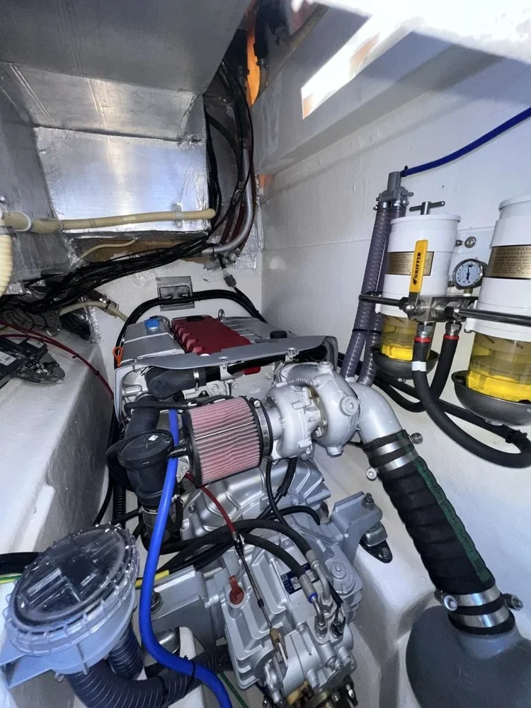 Close-up of a small boat engine with various hoses, filters, and wiring in a confined engine compartment.