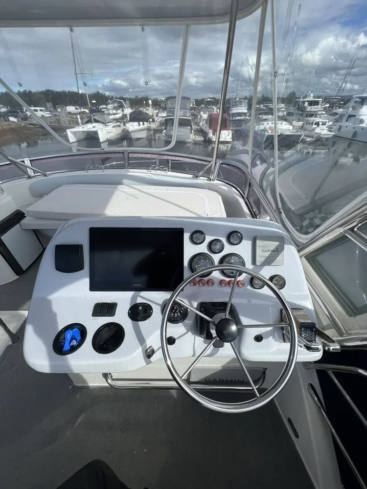 Boat control panel with steering wheel, GPS, and navigation instruments, overlooking a marina with numerous boats docked.