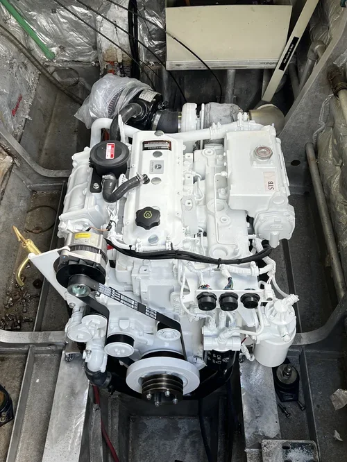 A white engine installed in a boat hull with visible pulleys, belts, and hoses, surrounded by boat components.