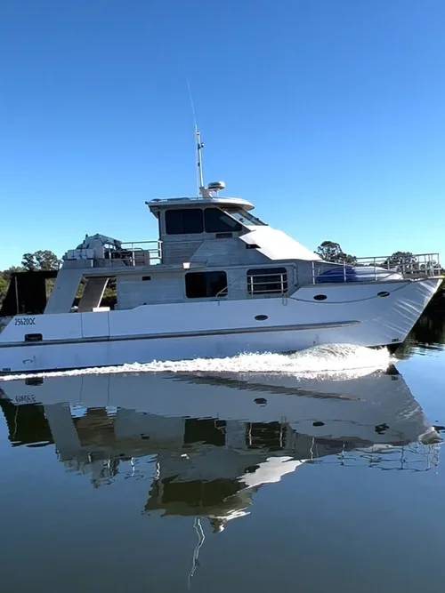 A white motor yacht cruising on calm water with a clear blue sky in the background.