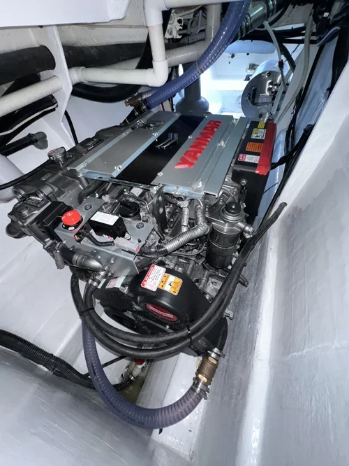 Marine engine with Yamaha branding installed in a boat engine compartment surrounded by white surfaces and various hoses and pipes.