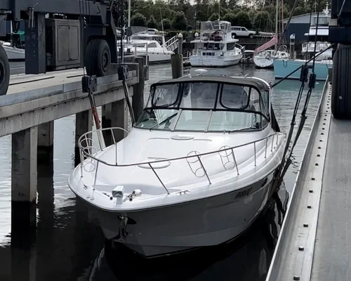 A white and black motorboat docked at a marina alongside a concrete pier, with other boats and yachts in the background.