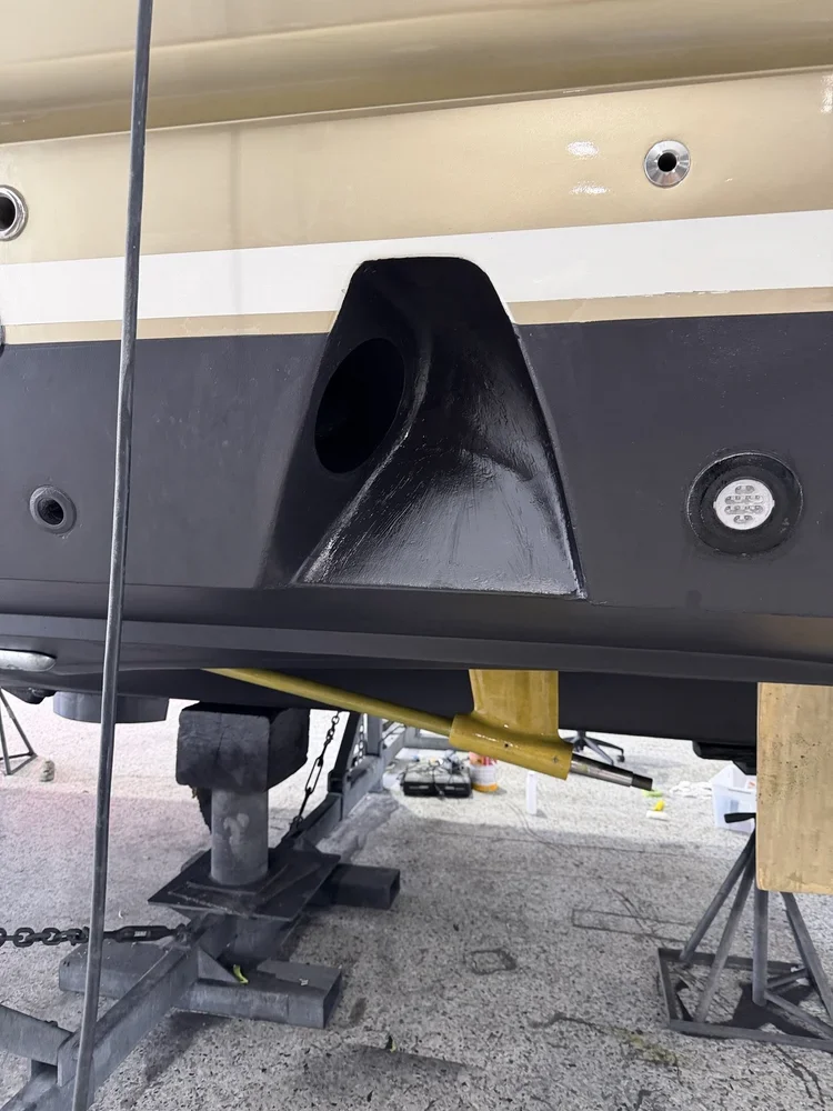 Close-up of a boat's hull with a large black opening for a propeller, supported on stands with tools nearby.