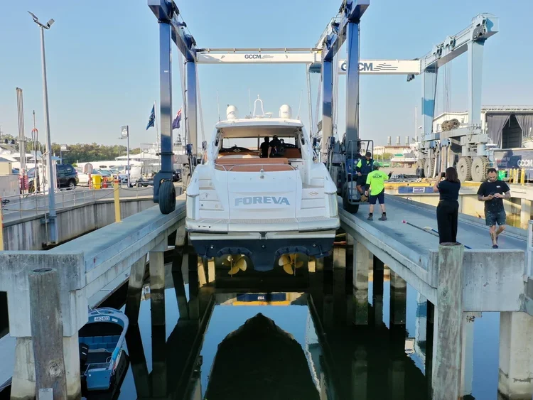 A luxury yacht named Foreva being lifted out of the water by boat hoists at a marina with people taking photos.
