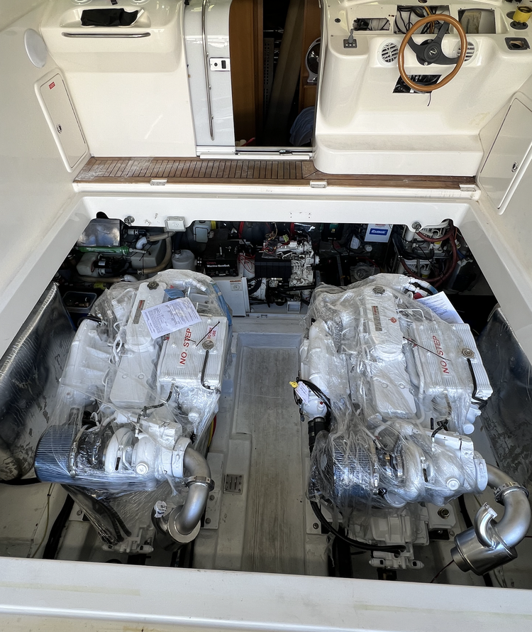 Two large engines wrapped in plastic in a boat engine compartment, with the boat's steering wheel and dashboard above.